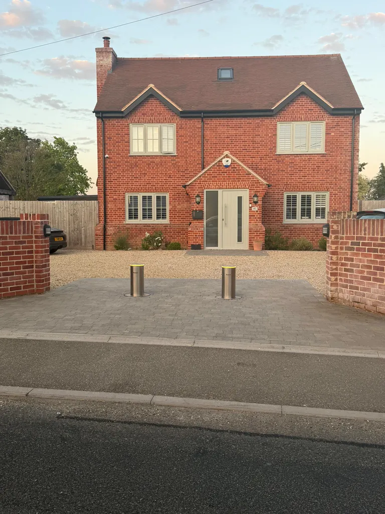 Two stainless steel bollards raised at dusk, guarding the entrance to a detached house