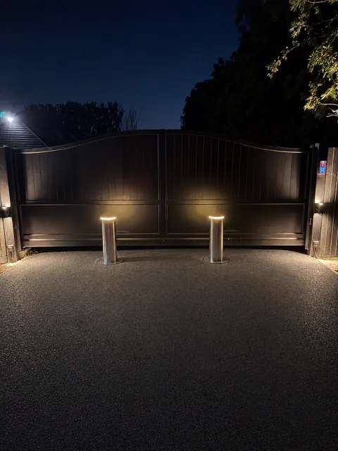 Two illuminated bollards raised at night in front of automatic timber driveway gates