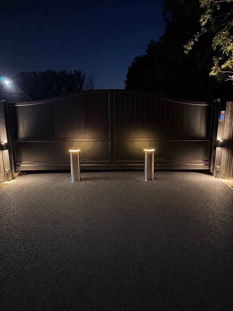 Two illuminated bollards raised at night in front of automatic timber driveway gates