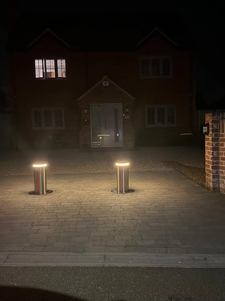 Two illuminated automatic bollards raised at night across a private driveway entrance