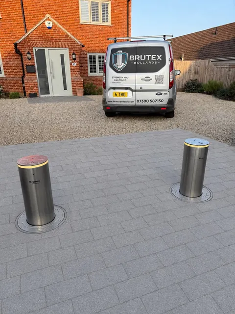 Two stainless steel Brutex bollards raised on a block-paved driveway, with the branded Brutex Bollards van parked behind