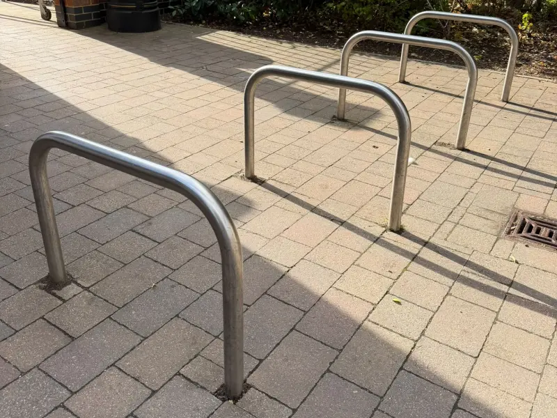 A row of stainless steel Sheffield cycle stands set into block paving